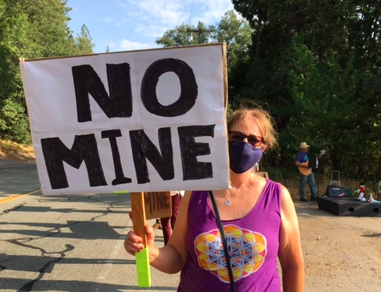 Woman wearing a face mask and holding a sign that says "NO MINE".